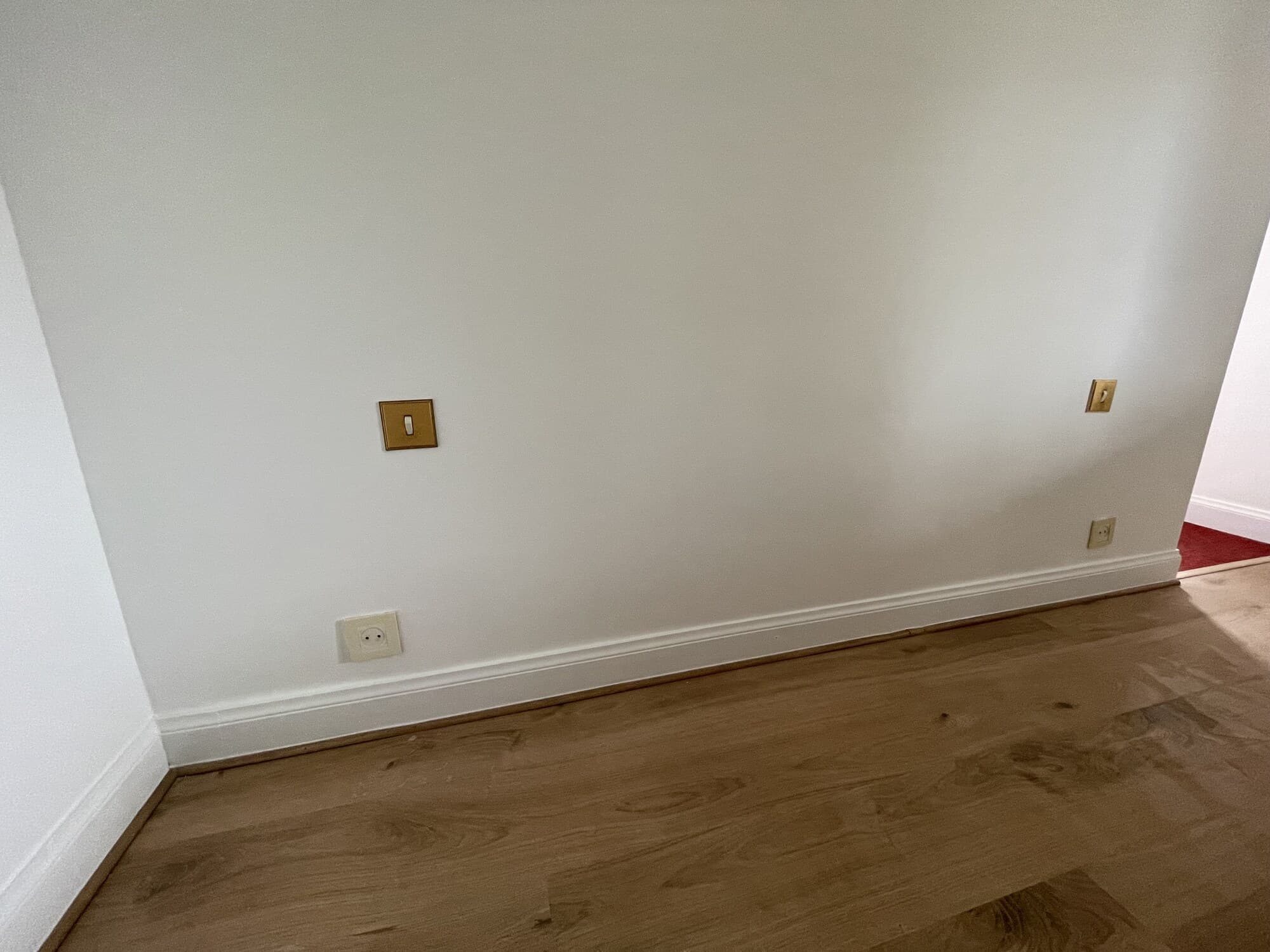Mur blanc avec parquet bois et interrupteurs en bronze