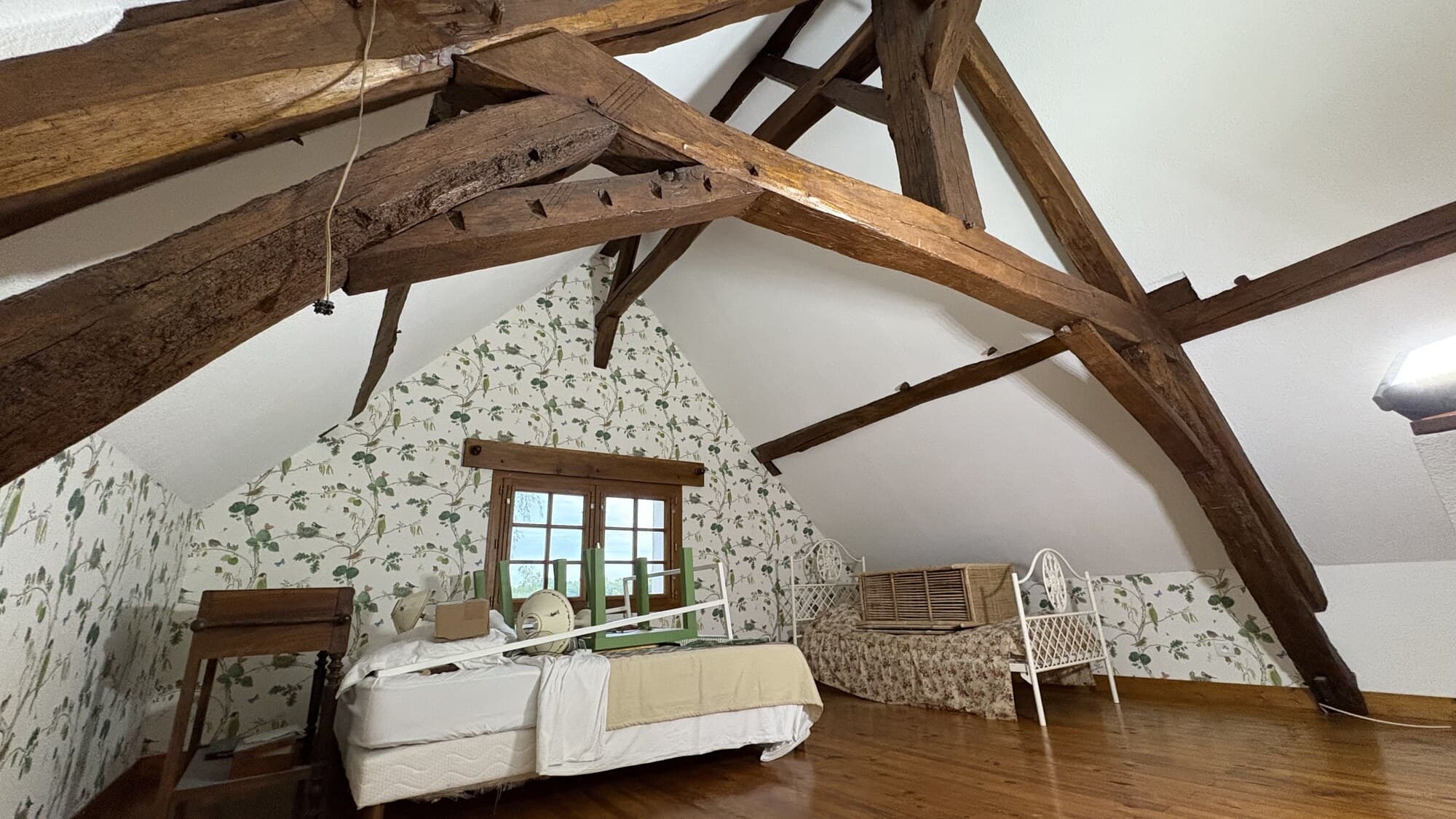 Chambre dans les combles, vue large avec lit et poutres