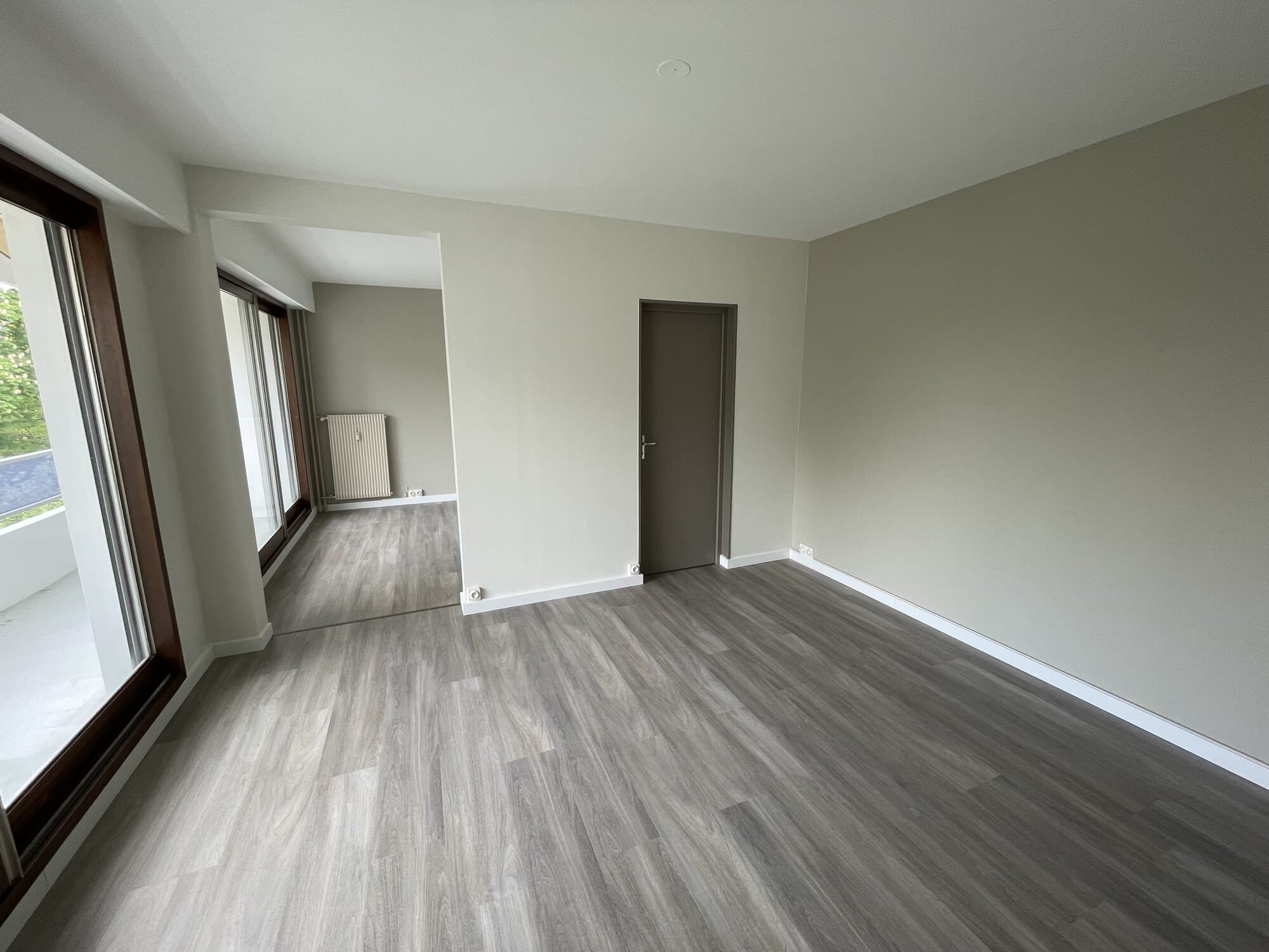 Grand séjour vide avec parquet gris et baies vitrées après peinture