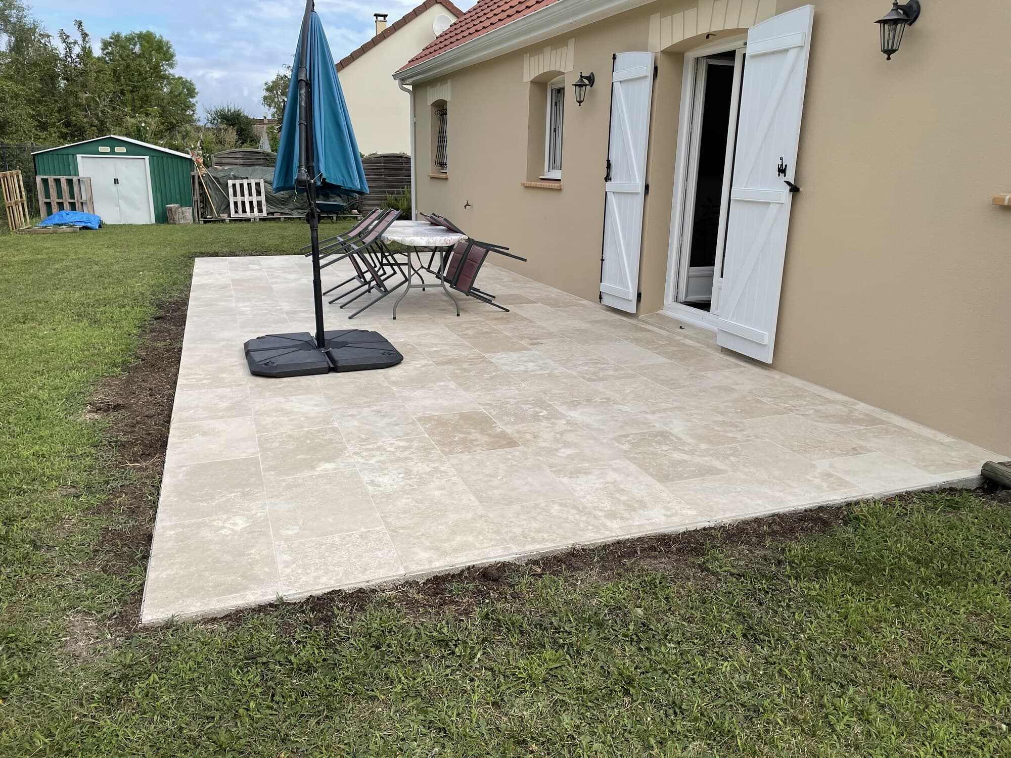 Terrasse en travertin avec parasol et chaises devant la maison