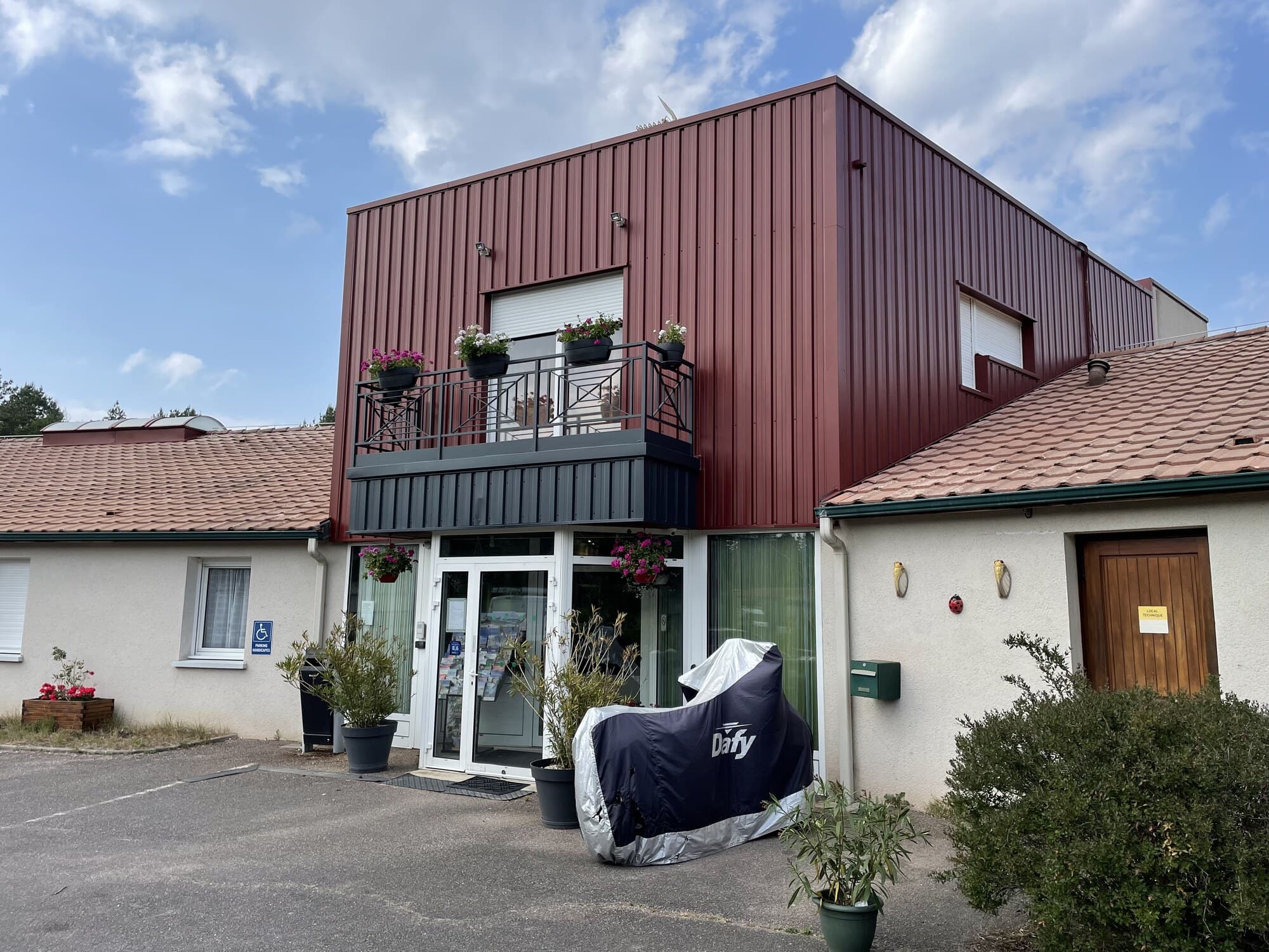Façade d'hôtel avec balcon fleuri et bardage rouge