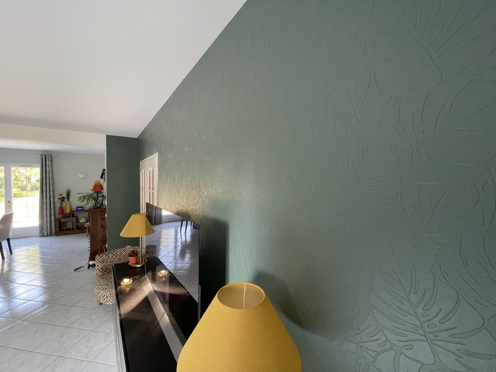 Salon avec mur vert tropical en relief feuillage et lampes design